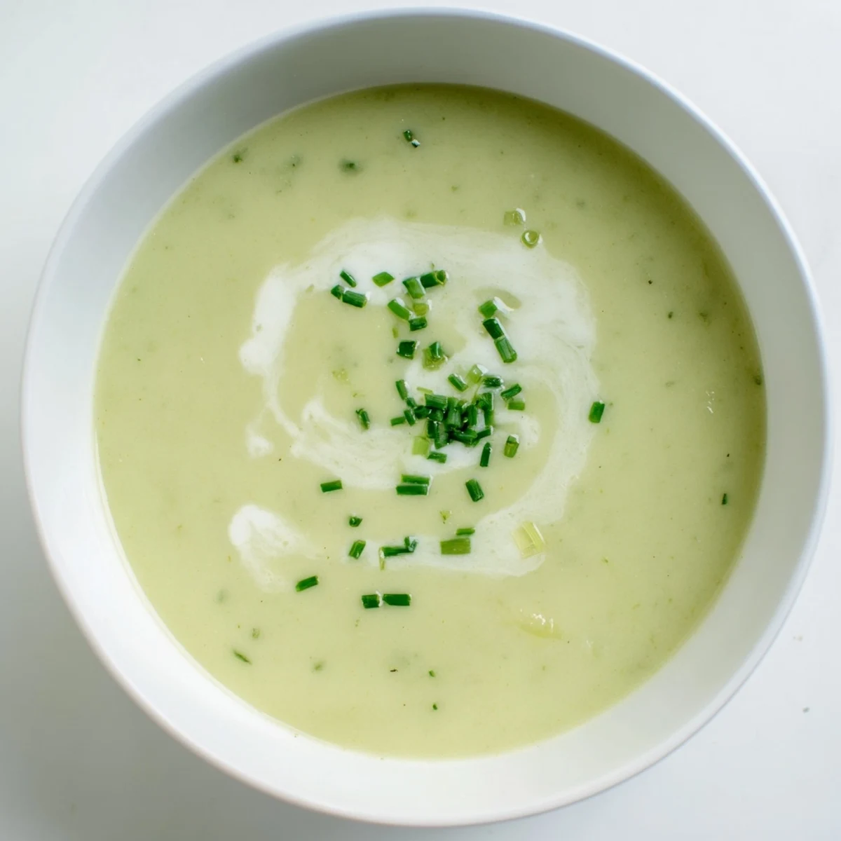 Warm bowl of Creamy Leek Soup, showcasing the ingredients and a swirl of cream.