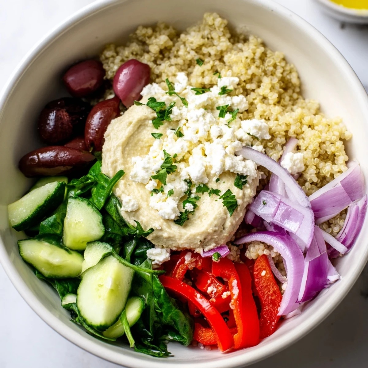 Bowl Méditerranéen au Quinoa avec Hummus et Olives, garni de légumes croquants et de feta.