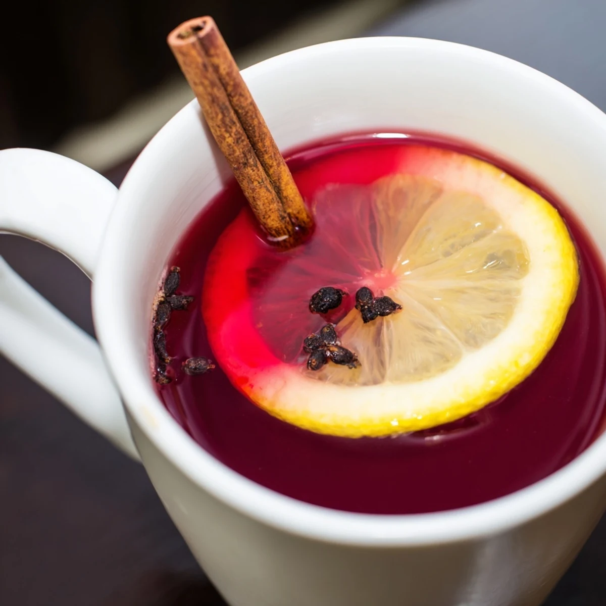 Freshly brewed Cranberry Tea with Lemon steaming in a clear glass mug beside sliced lemons and whole cranberries.