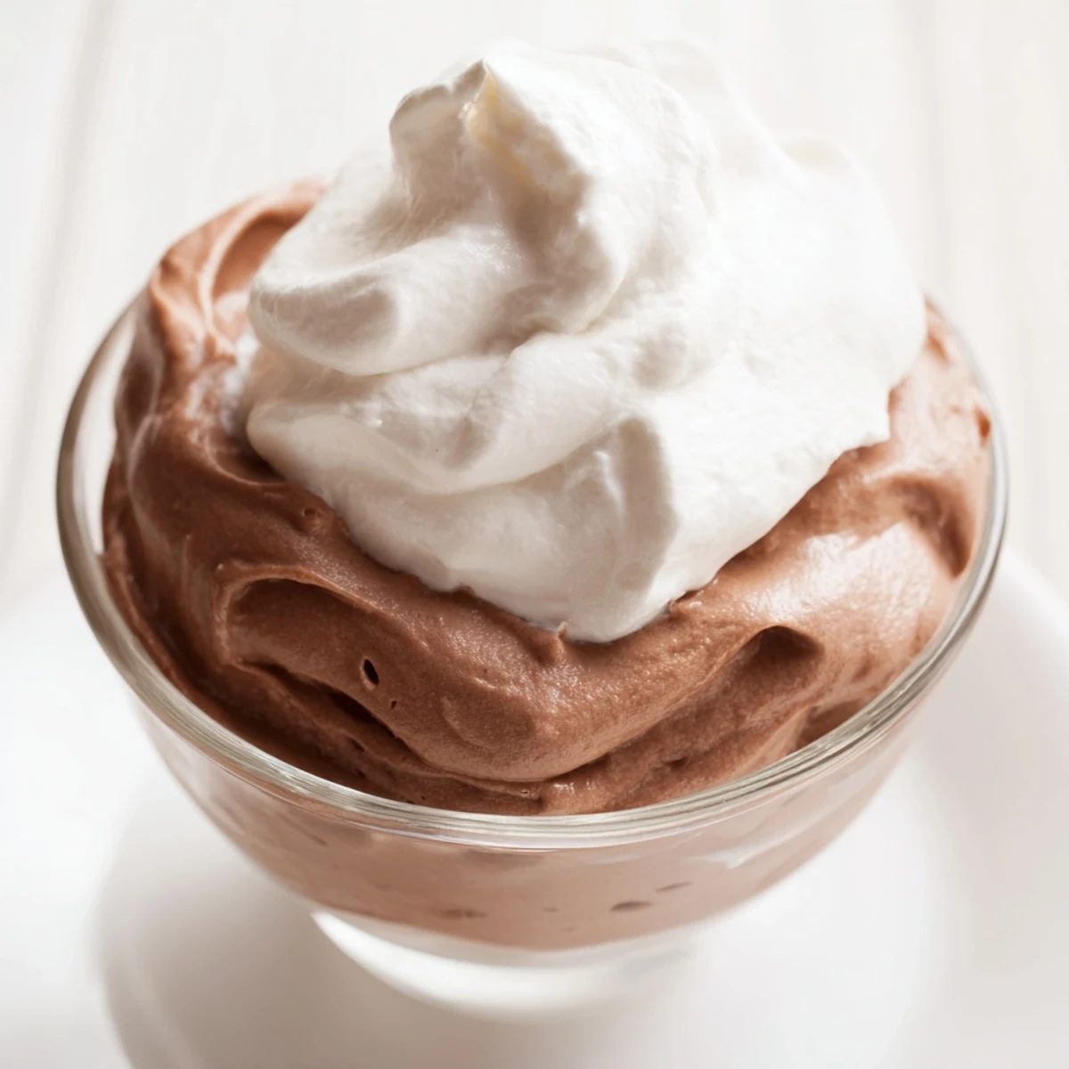 Mousse au chocolat fondante, présentée dans des verrines avec une garniture de crème fouettée et des éclats de chocolat.