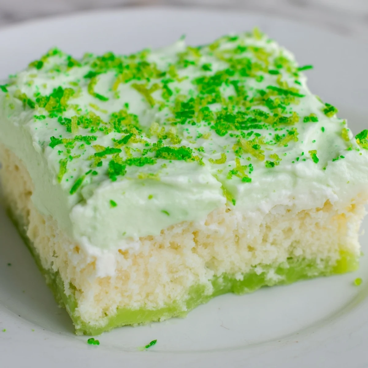 Le St. Patricks Day Lime Poke Cake est en vedette, un dessert gâteau américain cuit au four et décoré de zeste de citron vert et de paillettes.