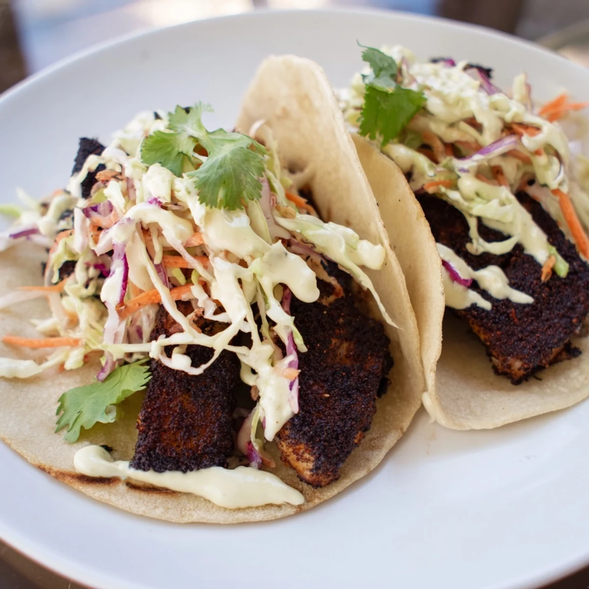 Serving plate of Louisiana Blackened Fish Tacos topped with crema, cilantro and lime wedges.