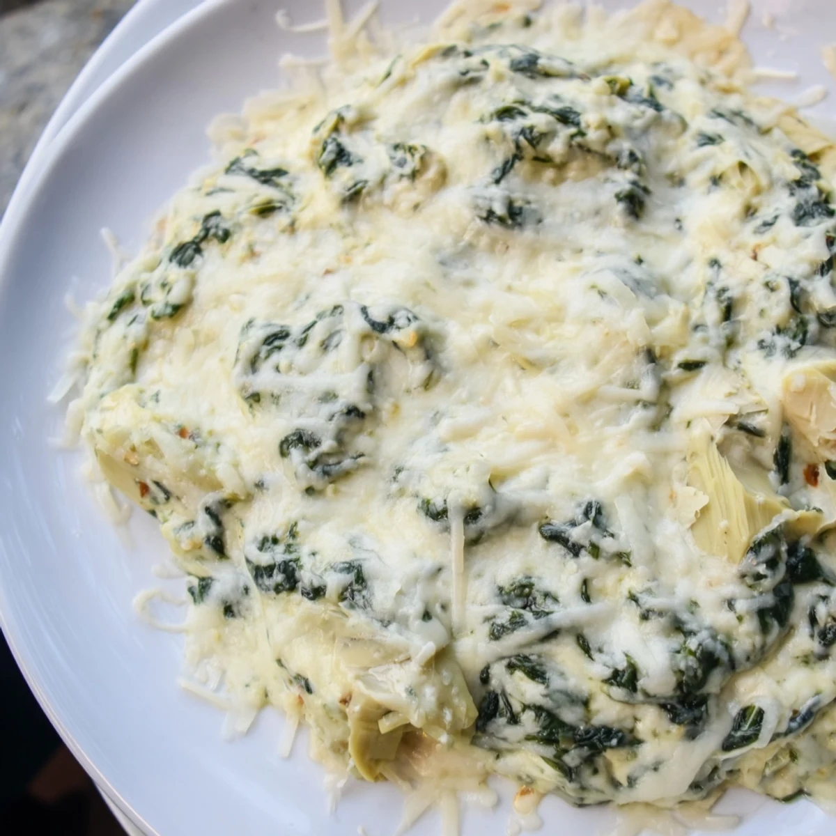 Présentation appétissante d'une Spinach and Artichoke Dip nappée de fromage et servie avec des légumes croquants pour un apéro sain.