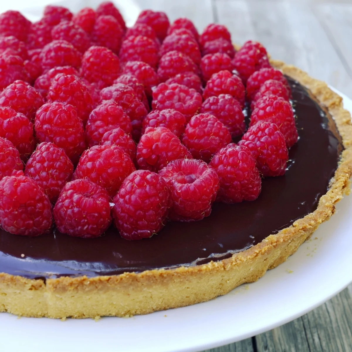 Une tarte au chocolat et framboises, une ganache onctueuse et des baies brillantes sur un fond de pâte sablée croustillante.