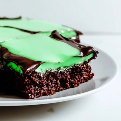 A stack of vibrant Green Mint Brownies topped with smooth mint frosting and glossy ganache, ideal for dessert.